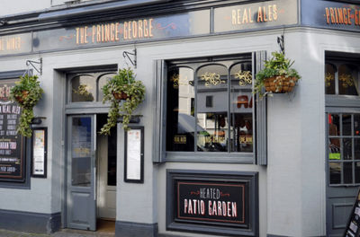 Exterior shot of the entrance of The Prince George. Displaying blooming hanging baskets against the grey and black paintwork.