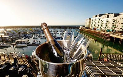 Lunch in Brighton, Brighton marina restaurants. A picture of an ice bucket with glasses on a wooden table overlooking the Brighton marina and the tall apartments to the left. Champagne is in the ice bucket. The sky is blue and it is sunny.