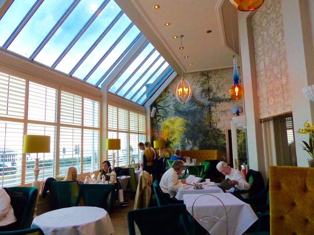 Floor to ceiling window terrace with tables and chairs and people dining.The Victoria Terrace at The Grand Hotel Brighton. A Brighton seafront restaurant