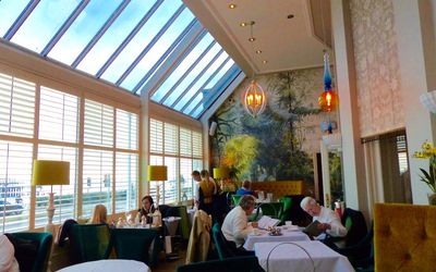 Floor to ceiling window terrace with tables and chairs and people dining.The Victoria Terrace at The Grand Hotel Brighton. A Brighton seafront restaurant