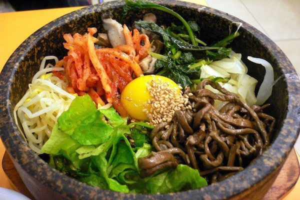 Oshio Brighton, a Korean Restaurant Brighton. Pictured a Korean salad with kimchi, noodles, carrot egg in the centre and sesame seeds. Served in a black bowl. 