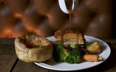 Roast pork with a Yorkshire pudding, broccoli, potatoes and gravy being poured over the dish