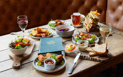 diner table laid out with seven different dishes including big sandwich, meat, beer and wine. Pubs in Hove guide, the Better Half.