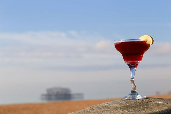 A bright red cocktail photographed on a wall with the beach in the background