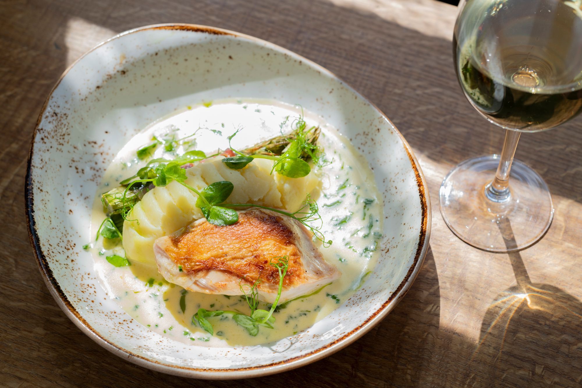 white bowl with puree and piece of meat served with glass of white wine