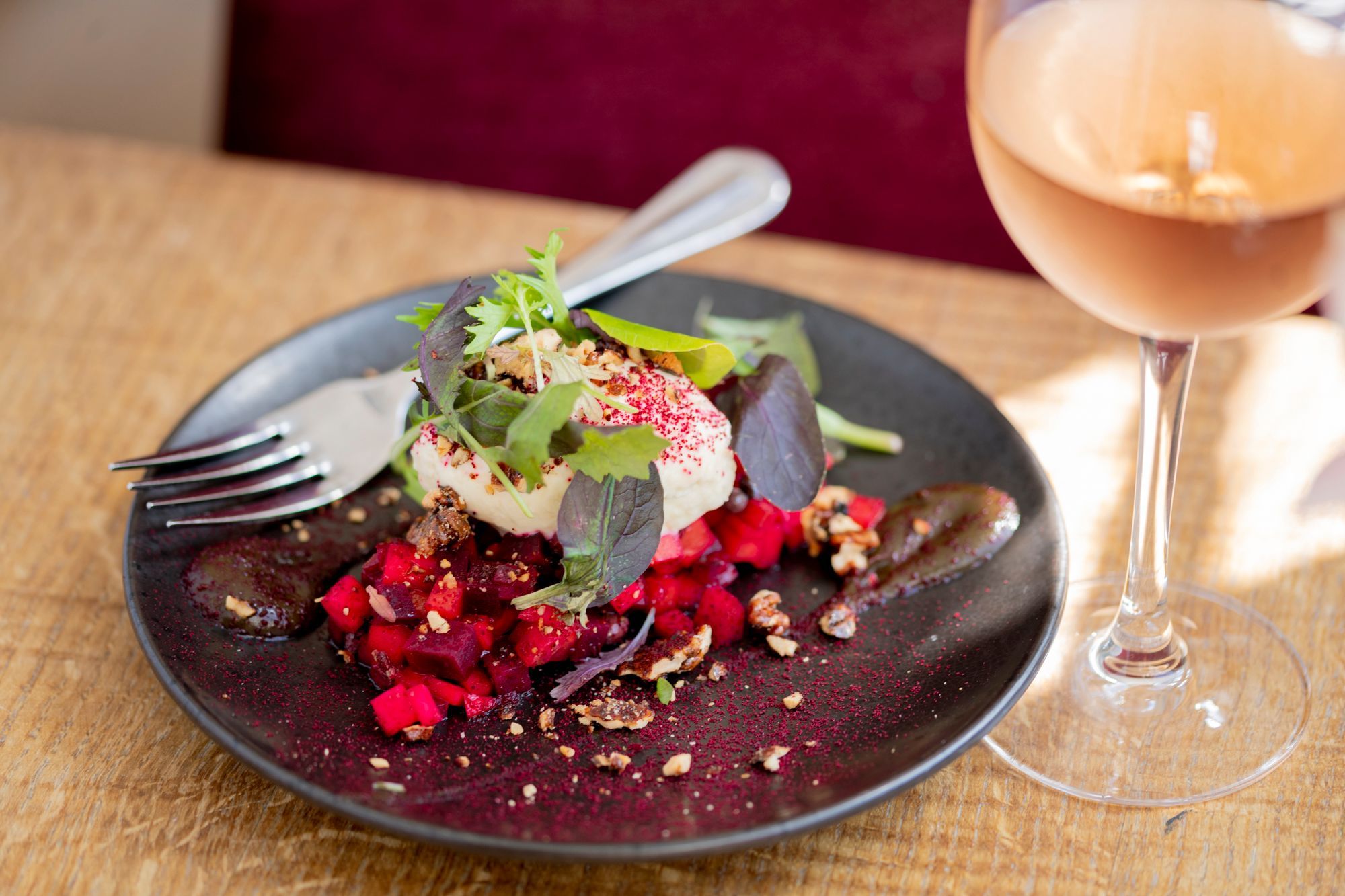 black plate with beetroot dish, served on the light brown table and with glass of white wine