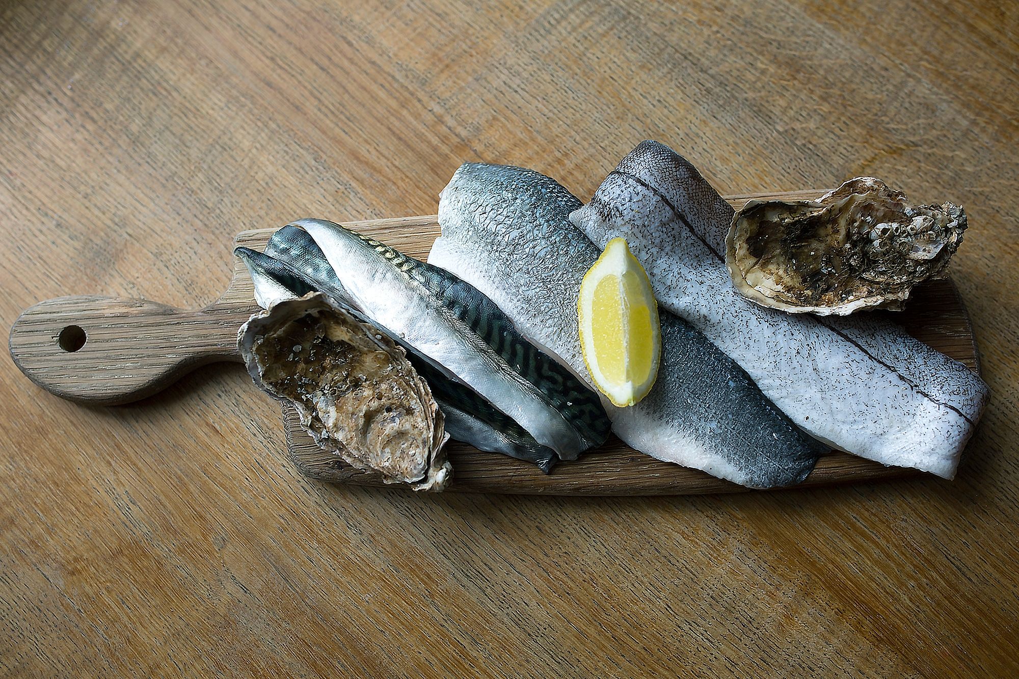 A wooden paddle with filleted fish and lemon
