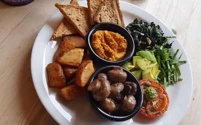 A vegan full english breakfast, avocado, wilted greens, grilled tomato, mushrooms, potato wedges and toast.