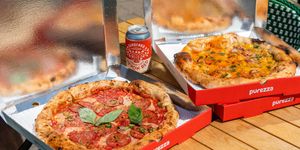 two open boxes of pizzas with the beer can next to it. Red pizza boxes on a wooden table. Vegan Brighton food