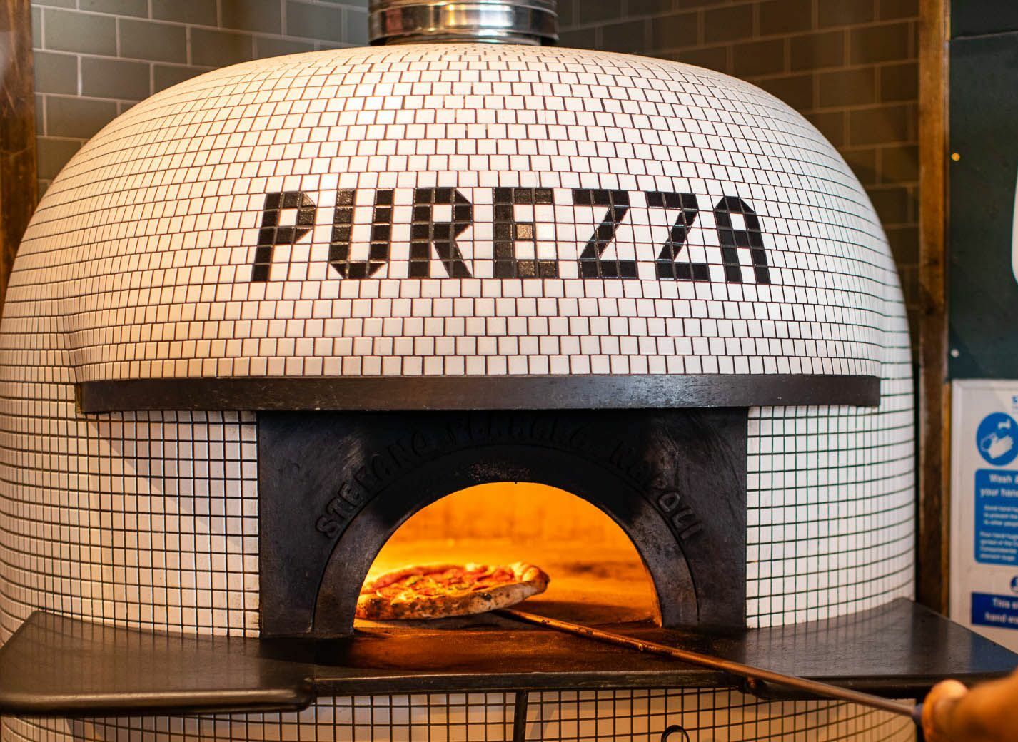 chef adding pizza into brick pizza oven