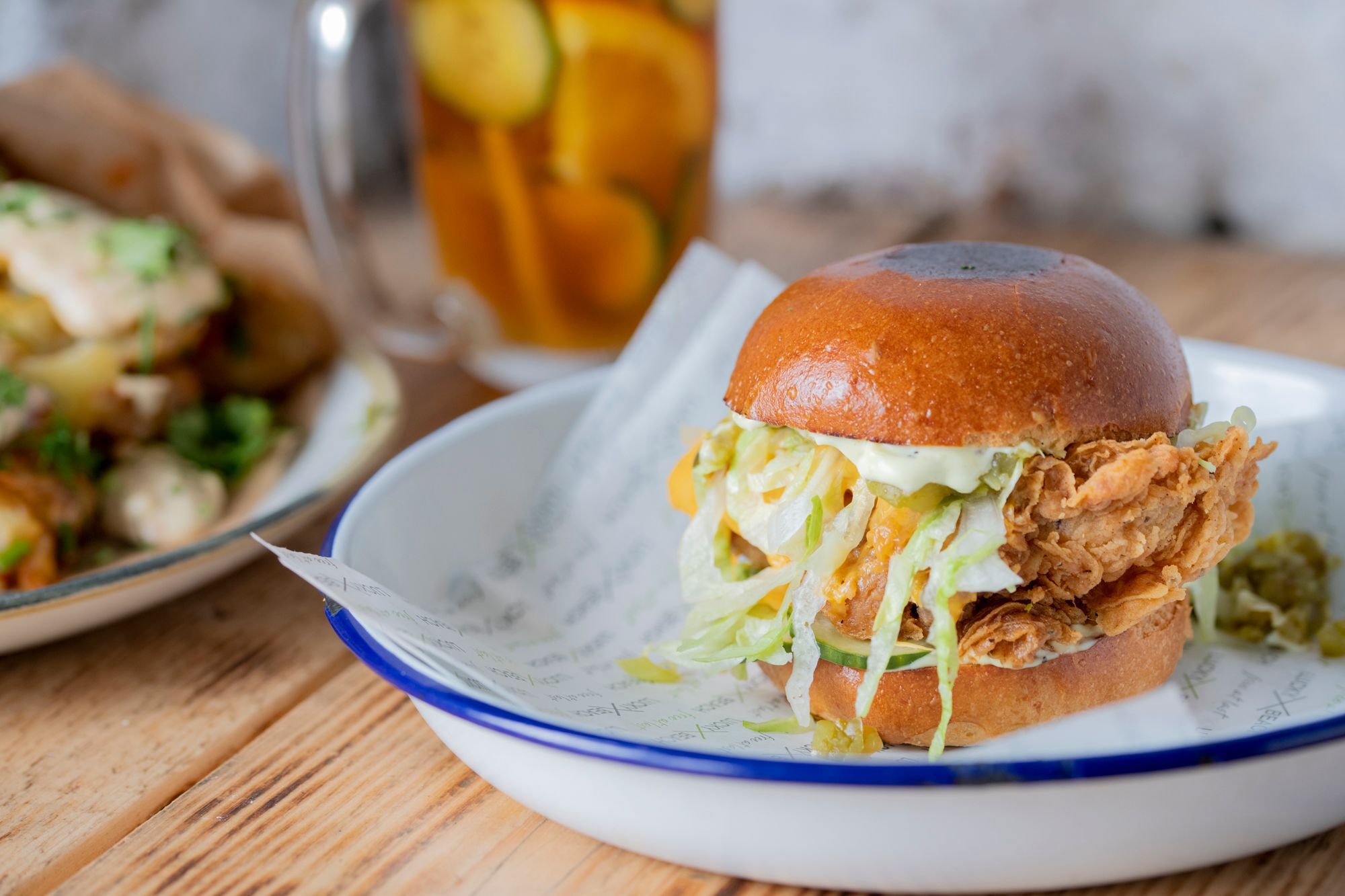 fish burger at Lucky Beach Brighton/ a close up picture with a classic looking white plate with a blue trim. relish and salad oozing out