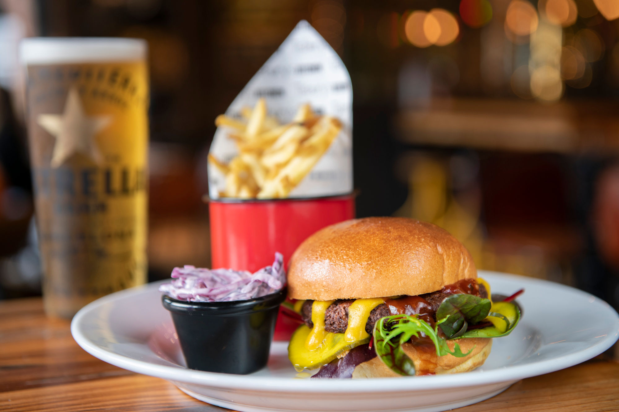 A cheeseburger with salad, a small pot of slaw and a cup of fries served on a white plate alongside a pint of beer.