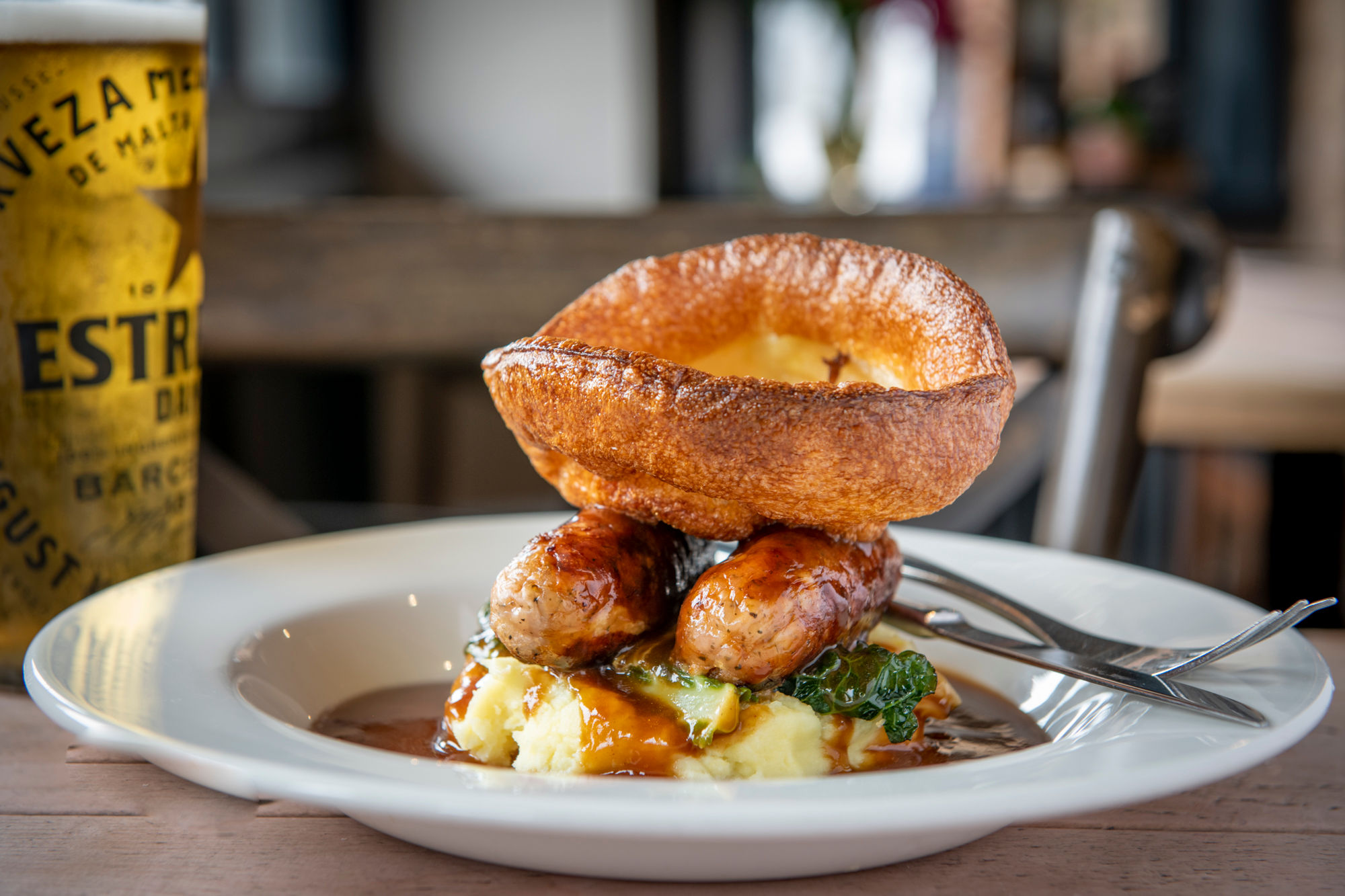 Two sausages on top of a pile of mashed potato with a large Yorkshire pudding. Serve with gravy on a white plate.