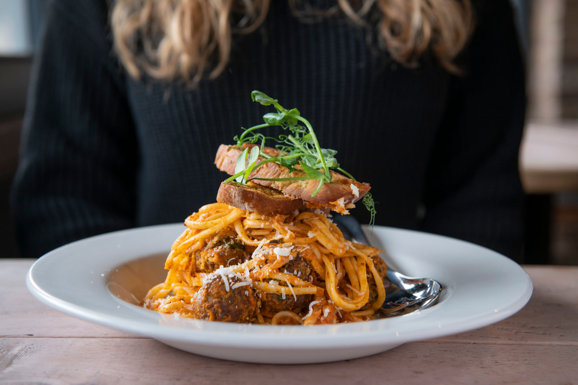 A bowl of spaghetti with meatballs and garlic bread. Garnished with microgreens.