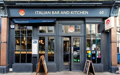 exterior shot of the Cin Cin restaurant in Hove, dark grey walls, window covered entrance and boards with informations. Cin is voted among the best restaurants in Brighton. Cin Cin • Modern Italian Dining in Hove