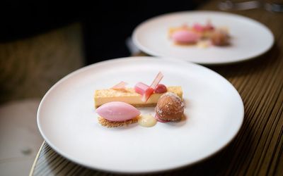 Desserts served on the table presented on large white plates. A donut ball, ice cream and rhuibarb.