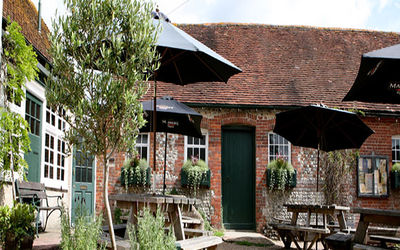 Exterior of red-brick pub with trees and black parasols on the tables.