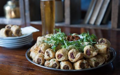 A large platter of sausage rolls garnished with fresh rocket laid out on a wooden table in preparation for a party.