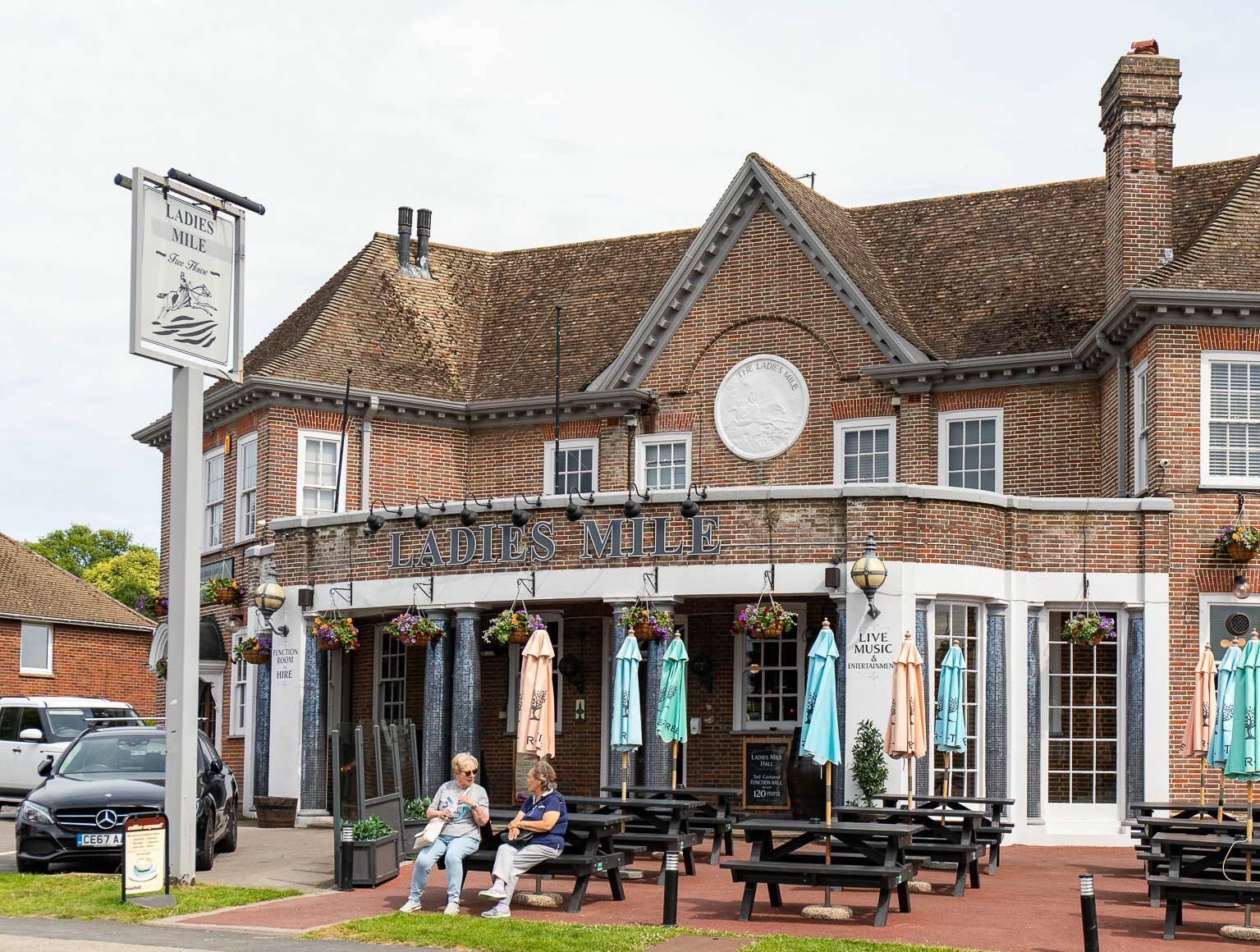 brown brick building of Ladies Mile in Patcham, black benches and tables, blue parasols 