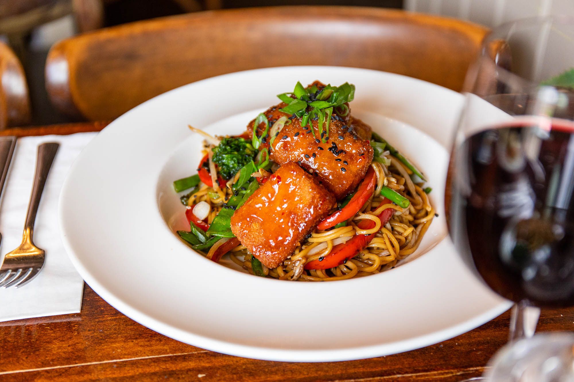 meat squares with noodles covered in sauce and served with glass of red wine