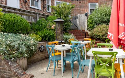 Lovely colorful part of garden at Ladies Mile, green, blue and orange chairs with white tables, red parasol, and lot of flowers