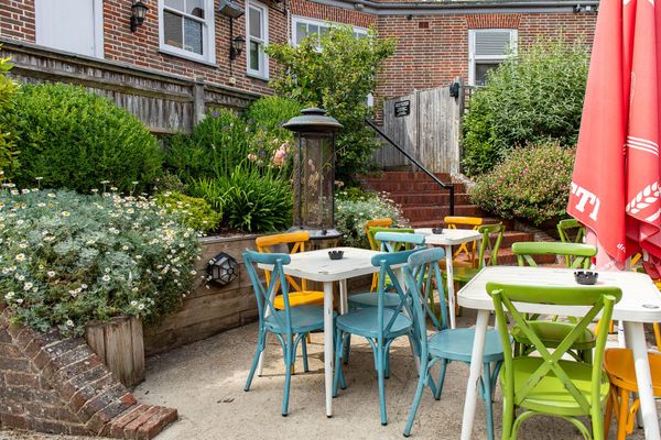 Lovely colorful part of garden at Ladies Mile, green, blue and orange chairs with white tables, red parasol, and lot of flowers