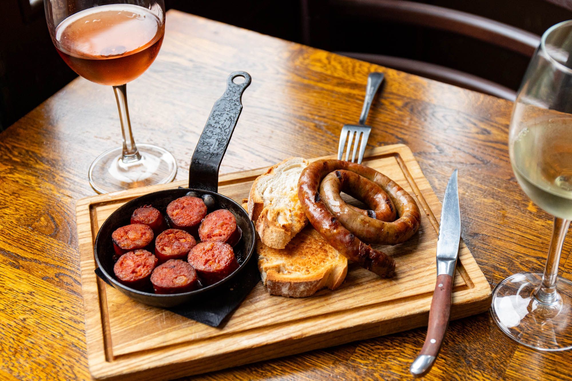 red sausage bits in the small black pan, and rolled sausage with bread served on the board and with glass of red