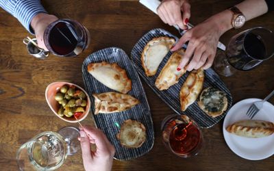 Overhead shot of wine and empanadas served on the dining table among friends sharing the tapas.