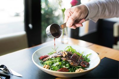 Steak salad with a sauce being poured over. Photographed next to a window with natural light.