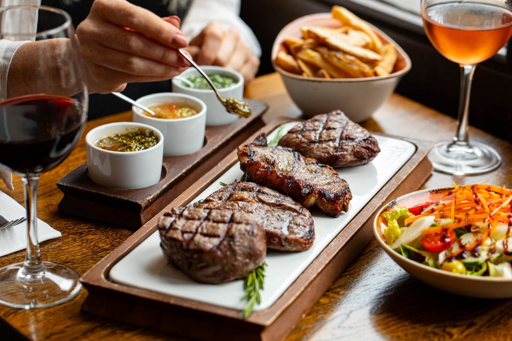 woman using kitchen made sauce to add it on the top of her steaks seven on white and brown board at LatinoAmerica