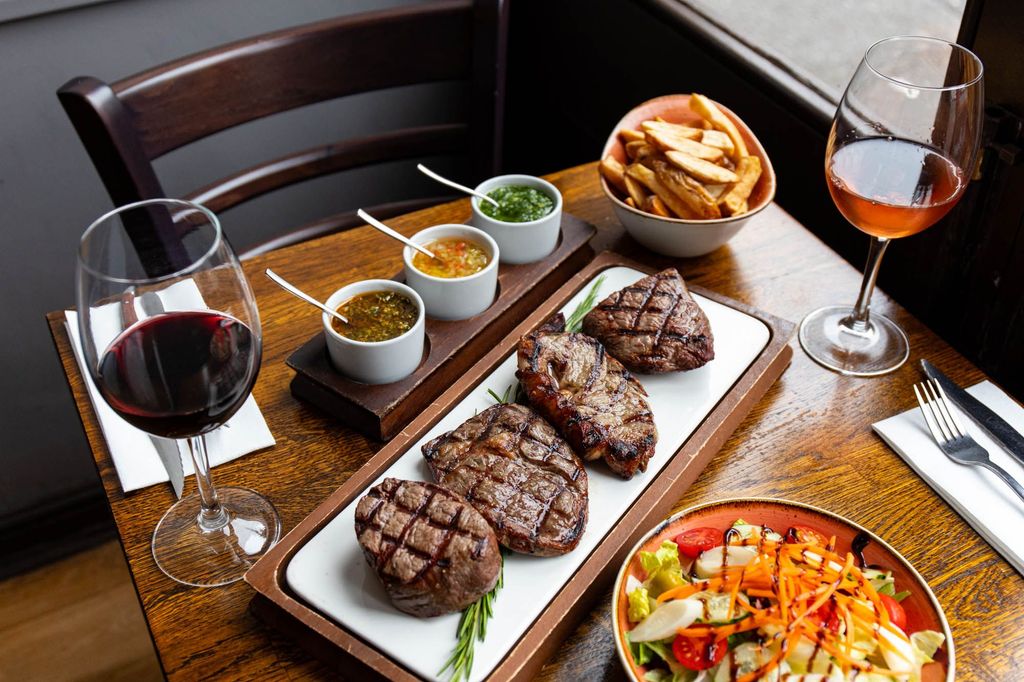 side shot of the brown wooden table at LatinoAmerica Hove, laid out with plate of Argentinian steak, different sauces, chips and salad