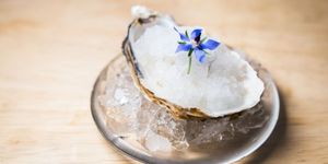 An oyster on a plate with crushed ice and an edible blue flower