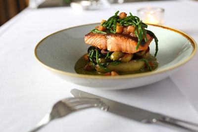 Salmon with samphire and a sauce, served in a shallow ceramic bowl on a white table cloth.