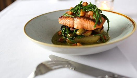 Salmon with samphire and a sauce, served in a shallow ceramic bowl on a white table cloth.