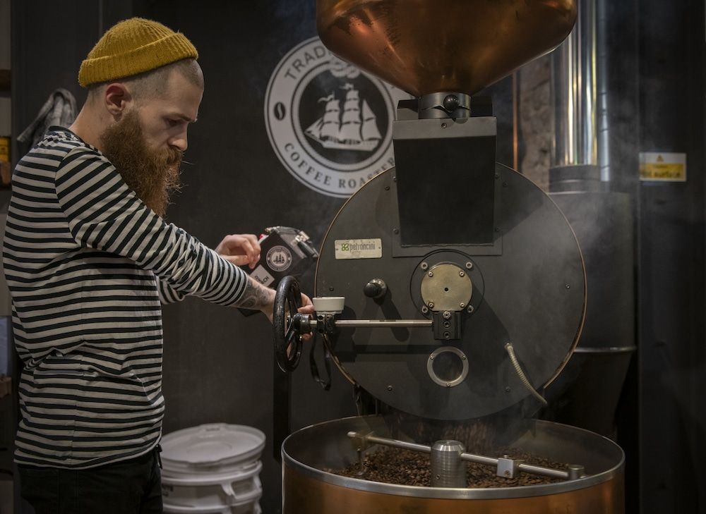 Trading Post Coffee. Brighton Coffee Shop Guide . A barista in a stripy top and beanie roasting coffee.