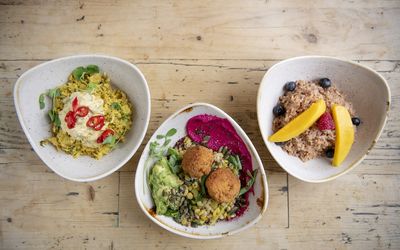 Triangular bowls of food including a bowl of porridge with fresh fruit, a bowl of salad with falafel and beetroot houmous.