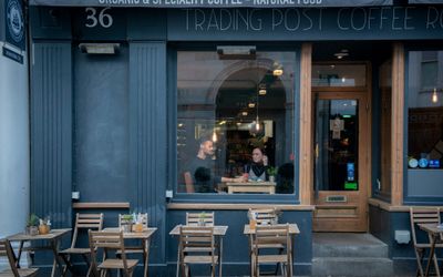 People sitting in the window drinking coffee with alfresco seating in front of them.