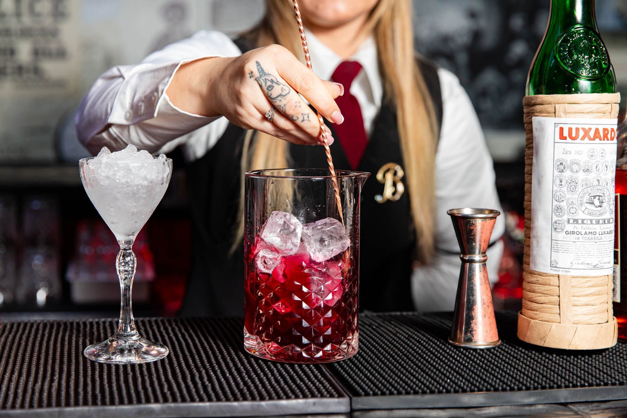a woman with unicorn tattoo on hand mixing and preparing a dark red cocktail at the Bohemia Brighton