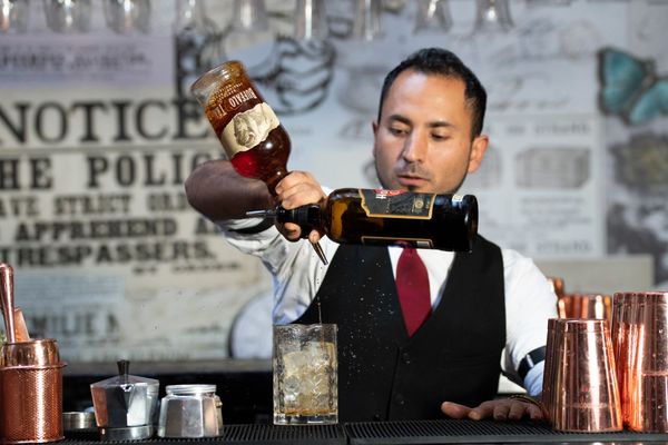 Bartender holding two bottles of alcohol with one hand and siping drinks into glass to make a cocktail