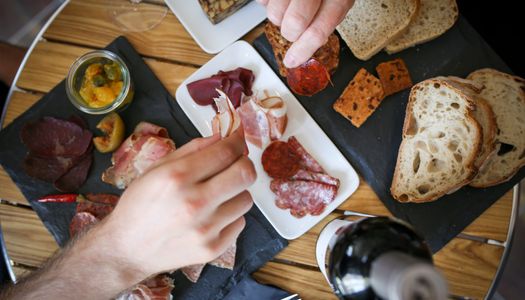 Sharing charcuterie platter served on slates with slices of bread and a bottle of wine.