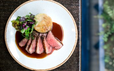 Sliced rare meat with fondant potatoes and a rich gravy. Served on a white ceramic plate with a brown glazed edge. Petit Pois is not a steak restaurant in Brighton, but the French know how to cook the best steak.