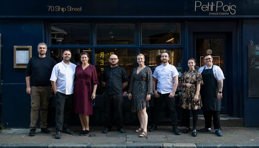 team photo of the Petit Pois team. 8 staff members elegantly dressed stood in front of the dark blue facade of the French bistro.