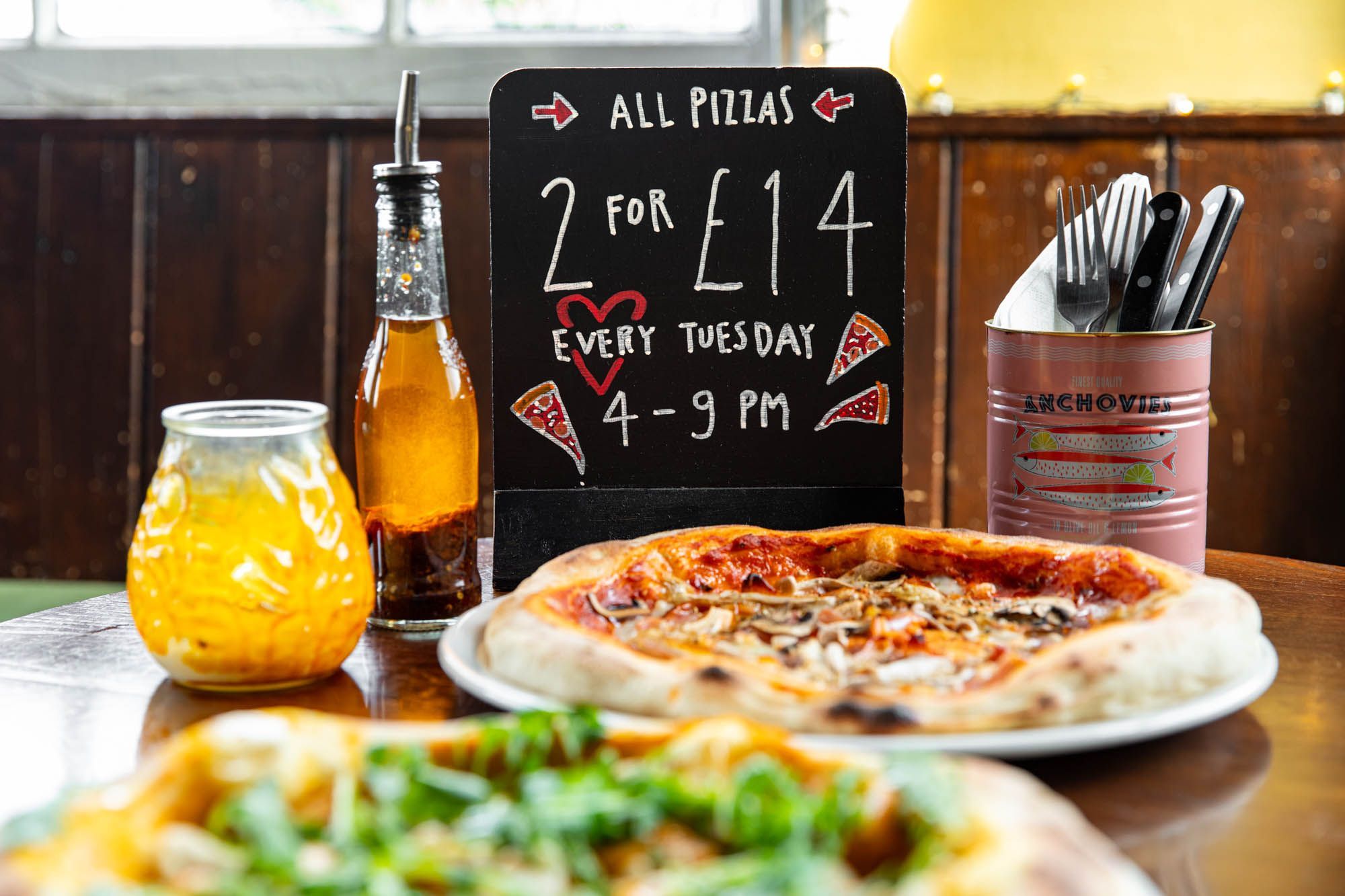 side shot of the meat pizza and mini black board with pizza offer, at The West Hill Tavern