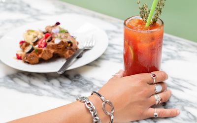 hand with rings on each finger holding bloody mary cocktail
