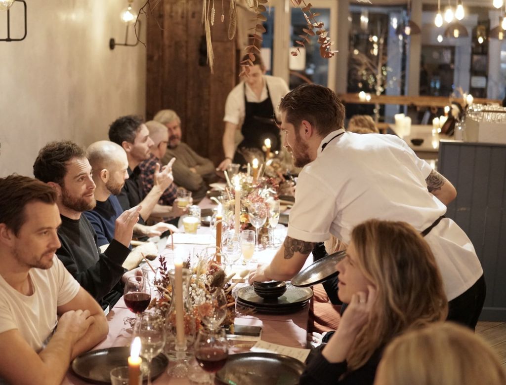 Guests at Lost Evenings at Lost in the Lanes Brighton, seated at a long table with chefs presenting them with dishes.
