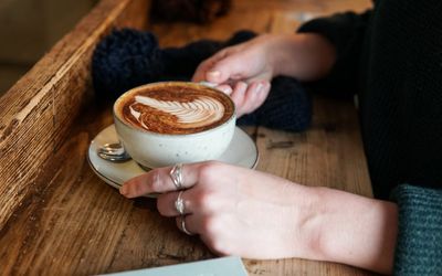 A woman's hands holding a cup of coffee on a wooden bench