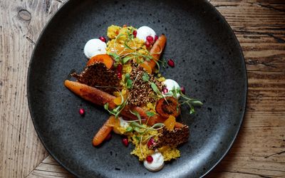 A black plate with miso carrots and pomegranate seeds