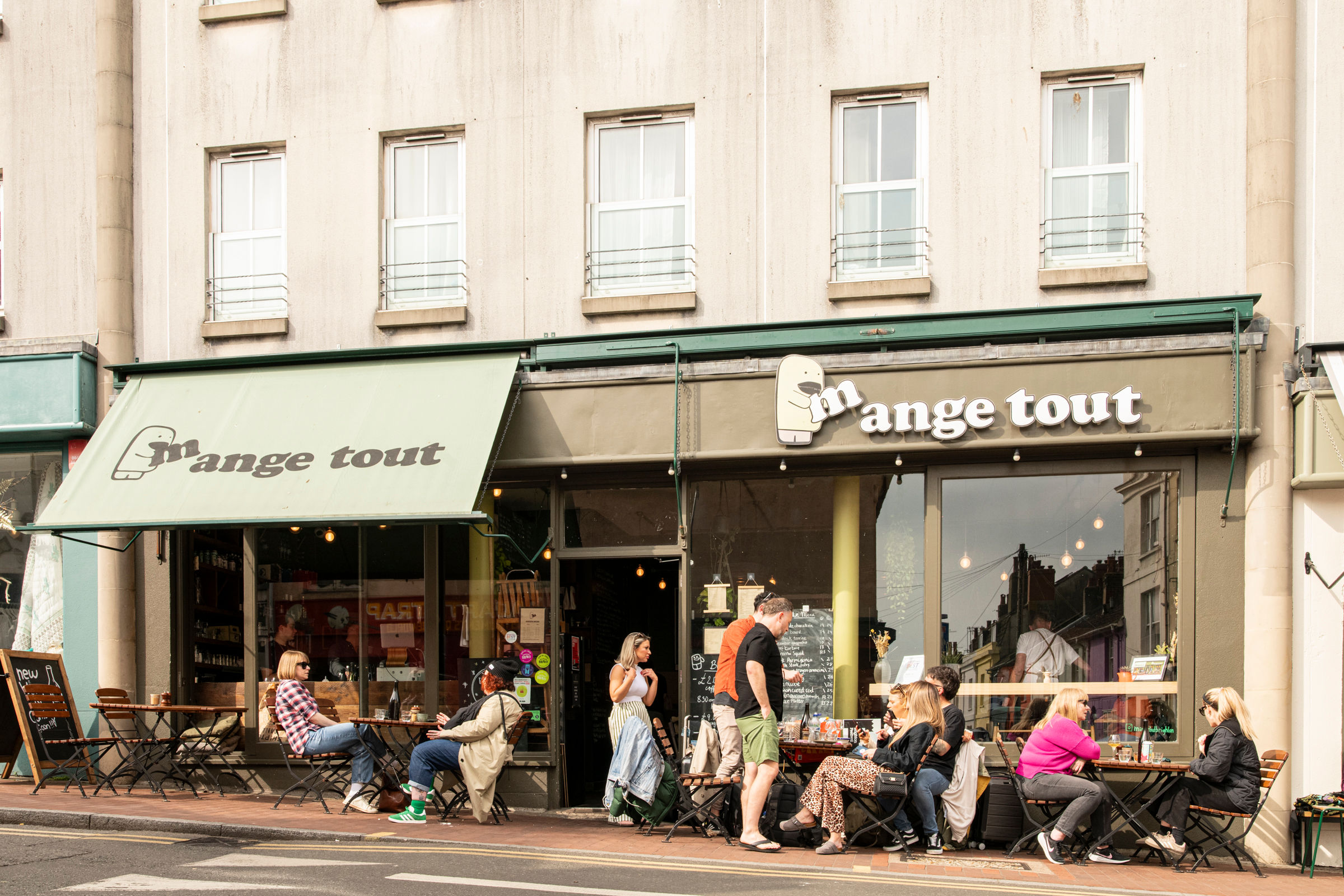 exterior shot of the Mange Tout Brighton cafe, people sitting in front of the venue, enjoying drinks and food in the sunshine