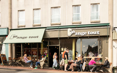 exterior shot of the Mange Tout Brighton cafe, people sitting in front of the venue, enjoying drinks and food in the sunshine