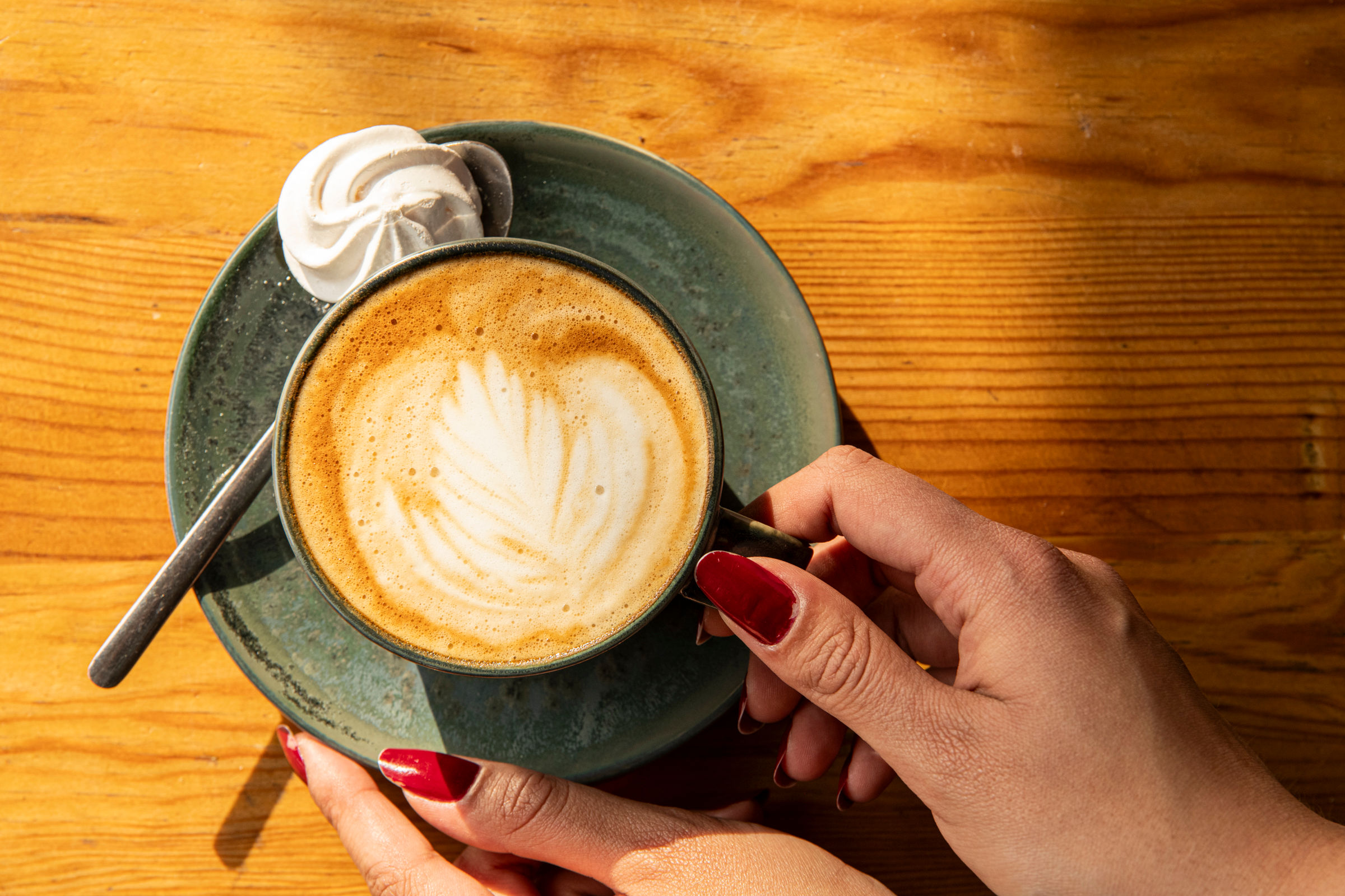 over head shot of the lady holding a cup of flat white coffee with the little sweet treat besides it